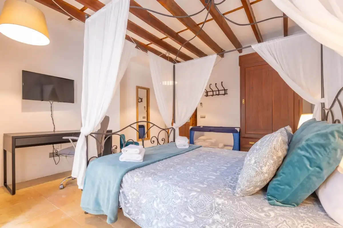 A bedroom with a canopied bed, white curtains, and exposed wooden ceiling beams.