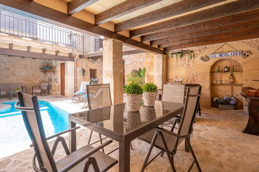 A covered patio with a dining table and seating beside a swimming pool.
