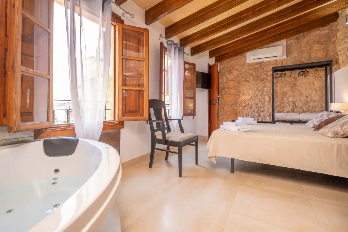 A bedroom with a bed, a freestanding bathtub, and wooden ceiling beams.