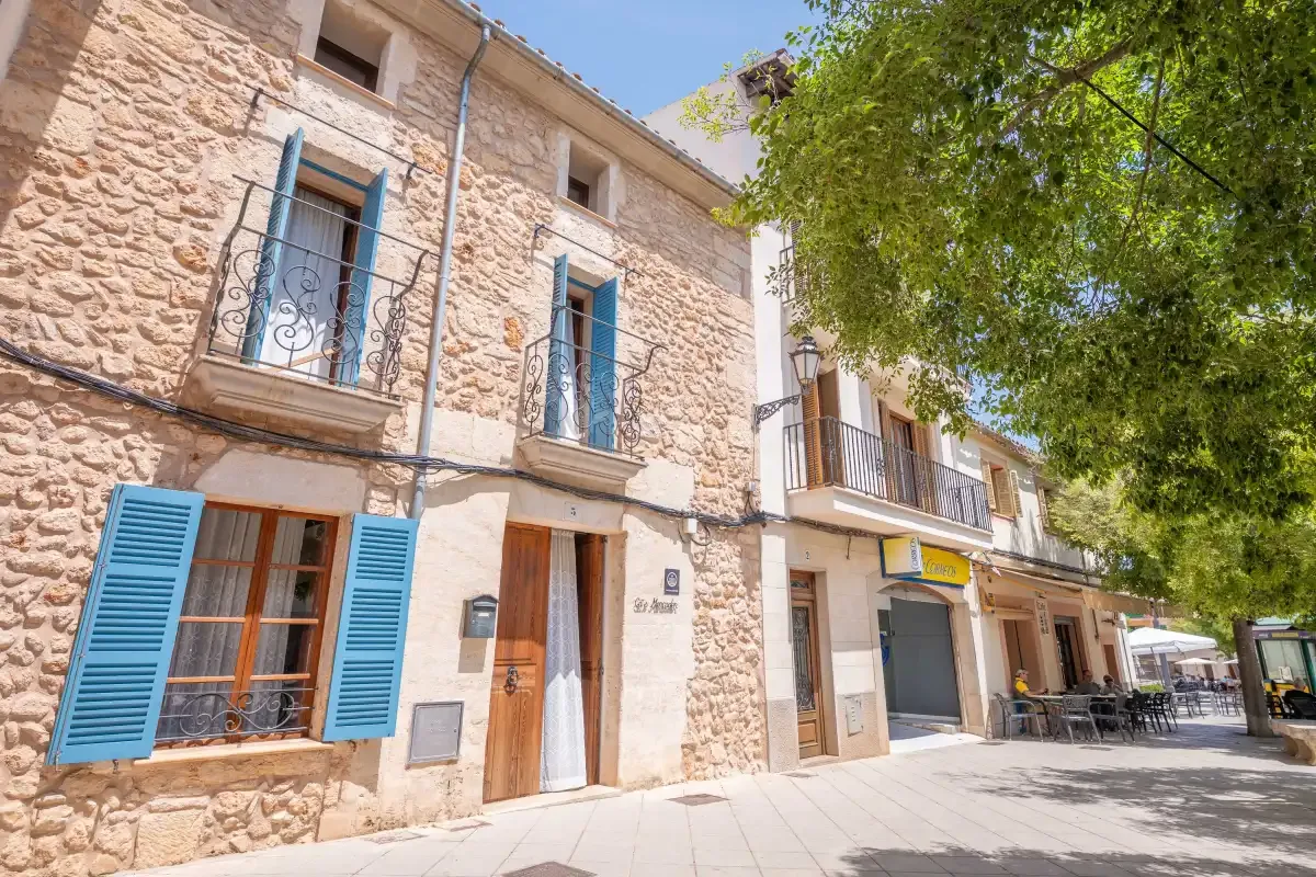 A stone building with blue shutters and balconies along a sunny street.