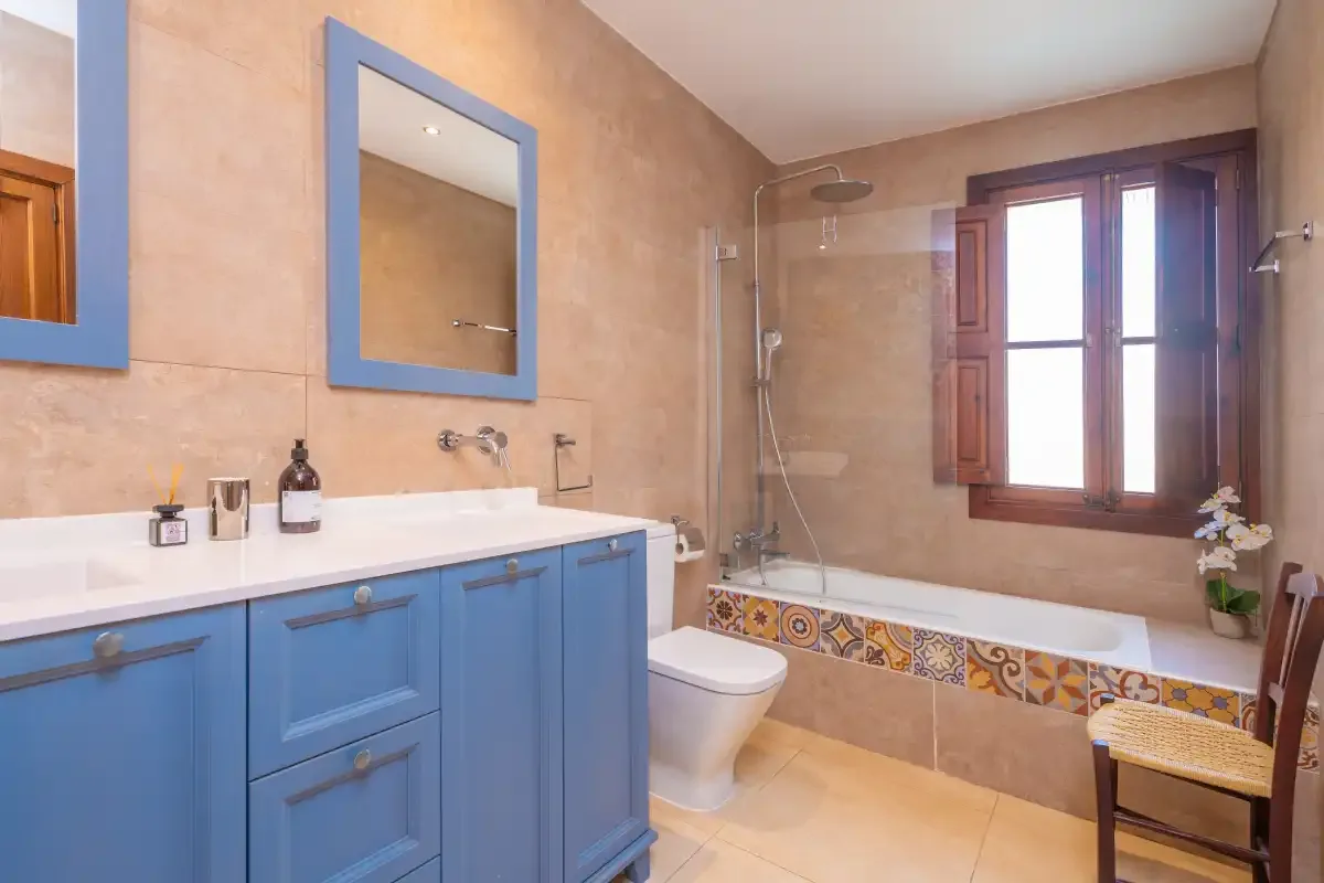 A bathroom with a blue vanity, bathtub, and window.
