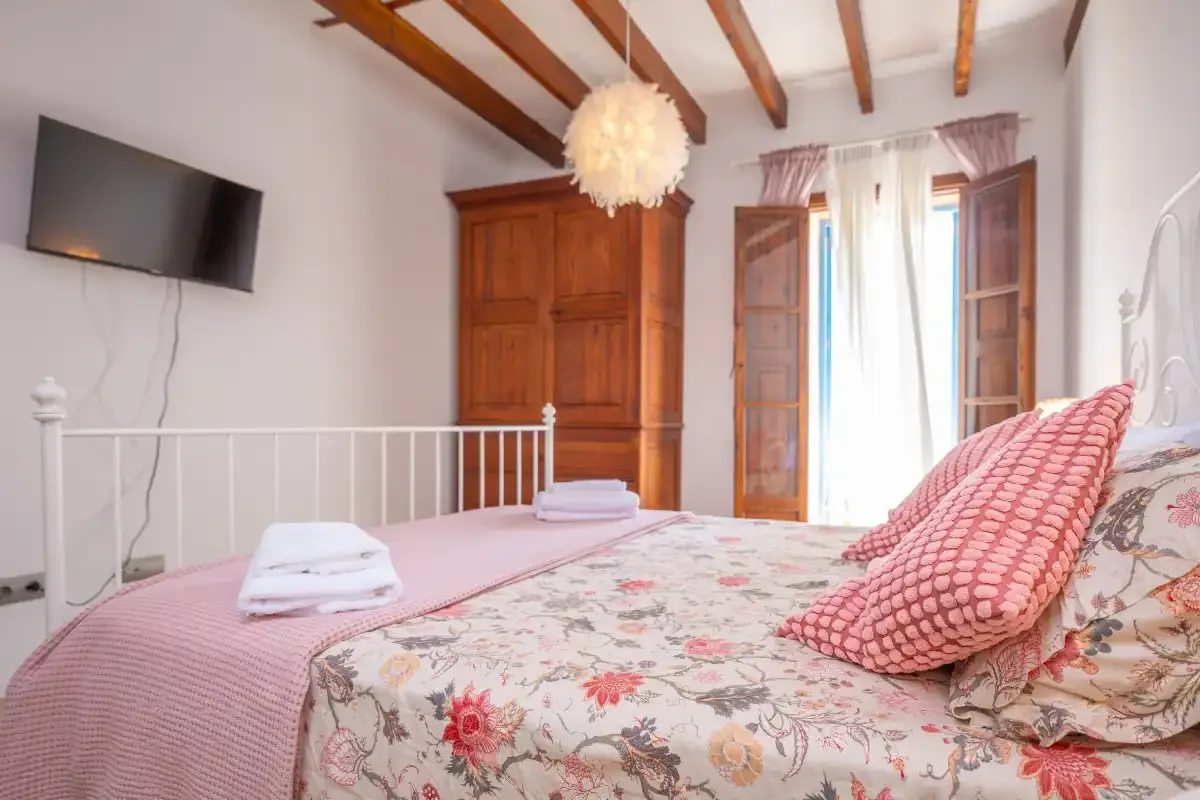 A bedroom with floral bedding, a wooden wardrobe, and a window.