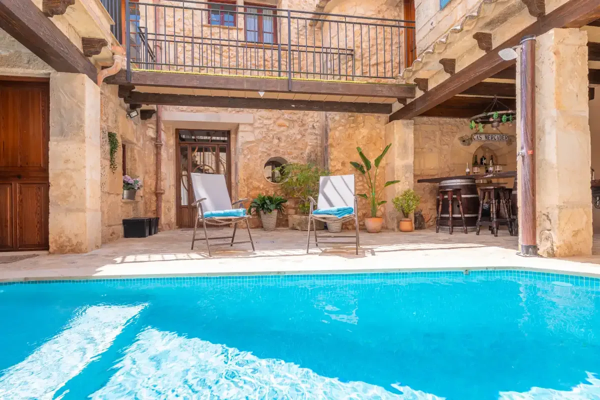 A courtyard pool sits beside a stone building with lounge seating and a bar.