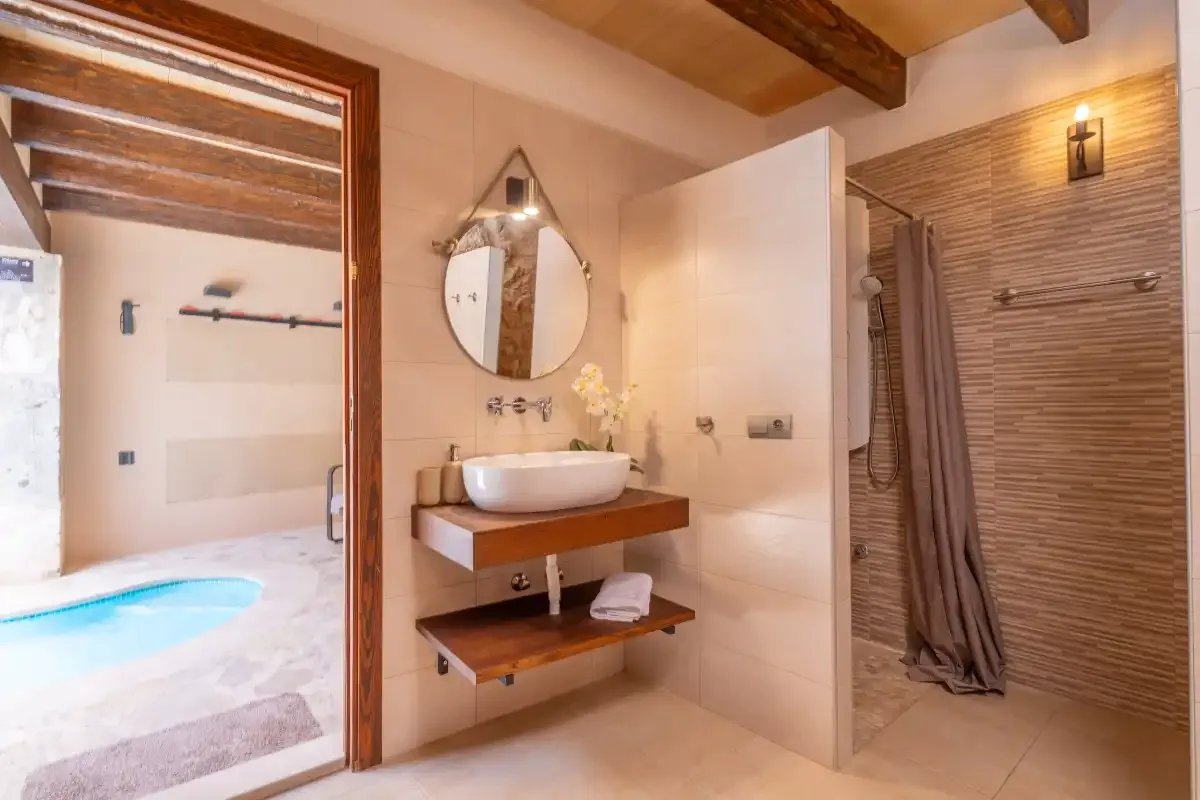 A bathroom with a wall-mounted sink, round mirror, and walk-in shower.