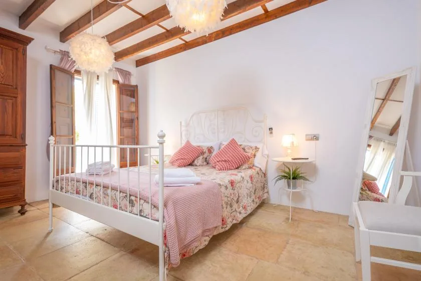 A bedroom with a white bed, pink bedding, and exposed wooden ceiling beams.