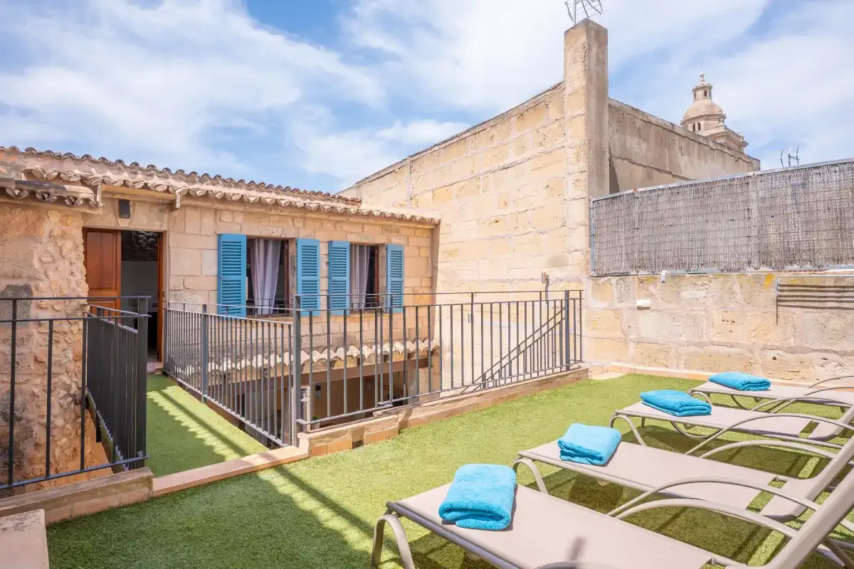 A sun terrace with lounge chairs sits beside a stone building with blue shutters.