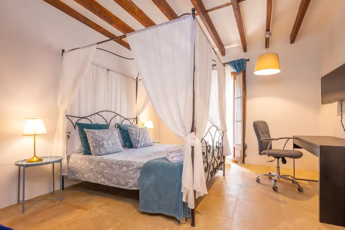 A bedroom with a canopy bed and a desk beside the window.