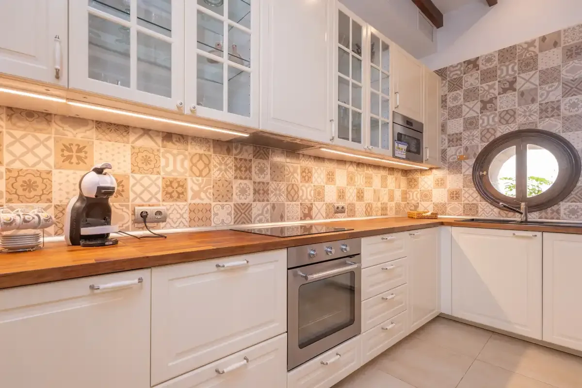 A bright kitchen with white cabinets, a wooden countertop, and patterned tile backsplash.