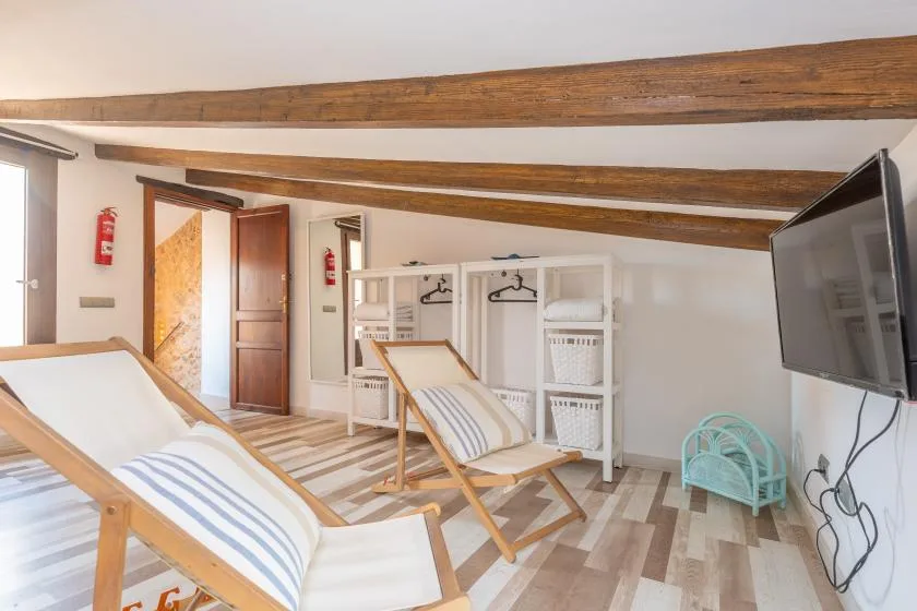 A bright attic room has reclining seating, open storage, and exposed wooden beams.