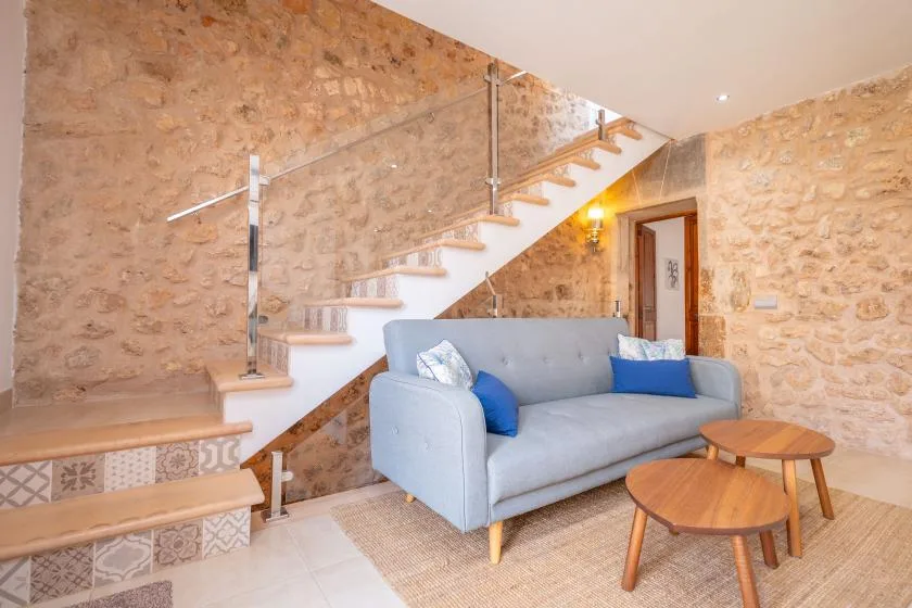 A living area with a gray sofa and a staircase against stone walls.
