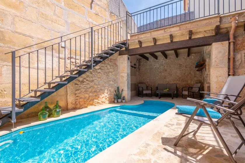 A courtyard pool sits beneath an outdoor staircase, with seating in the shaded alcove.
