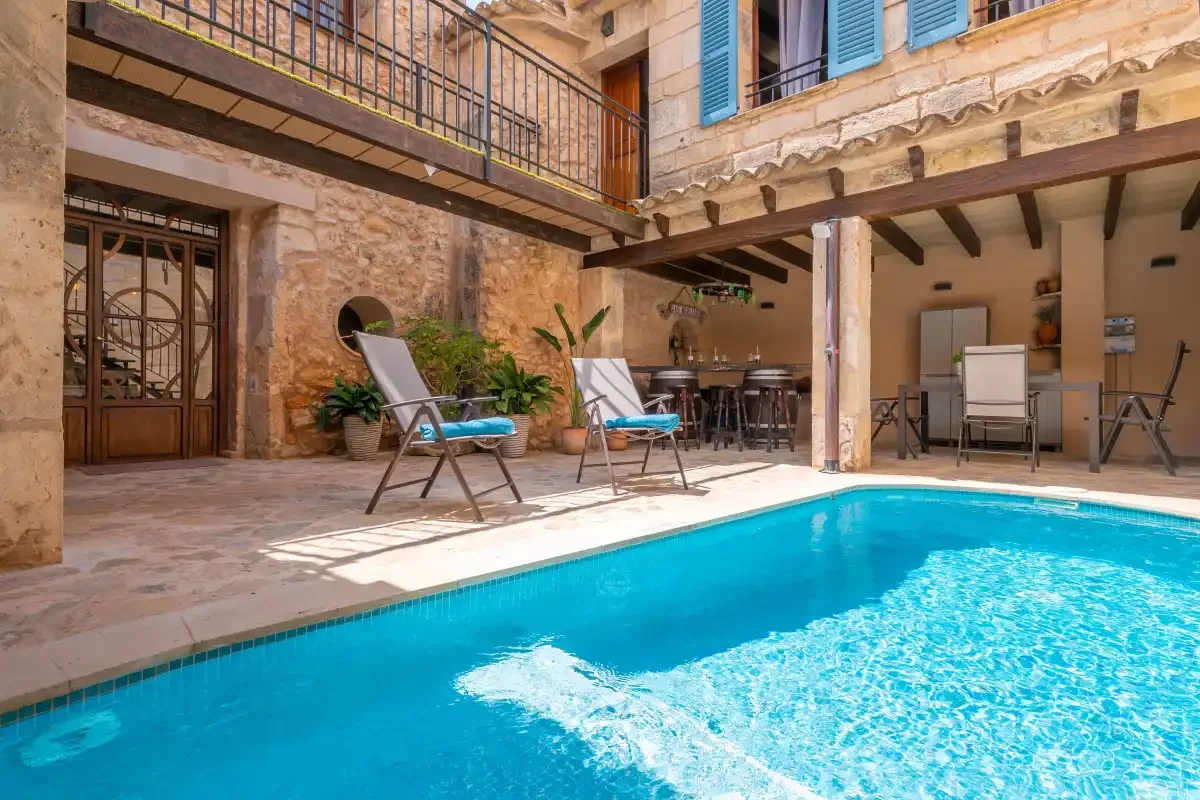 A courtyard swimming pool sits beside a stone building and shaded seating area.