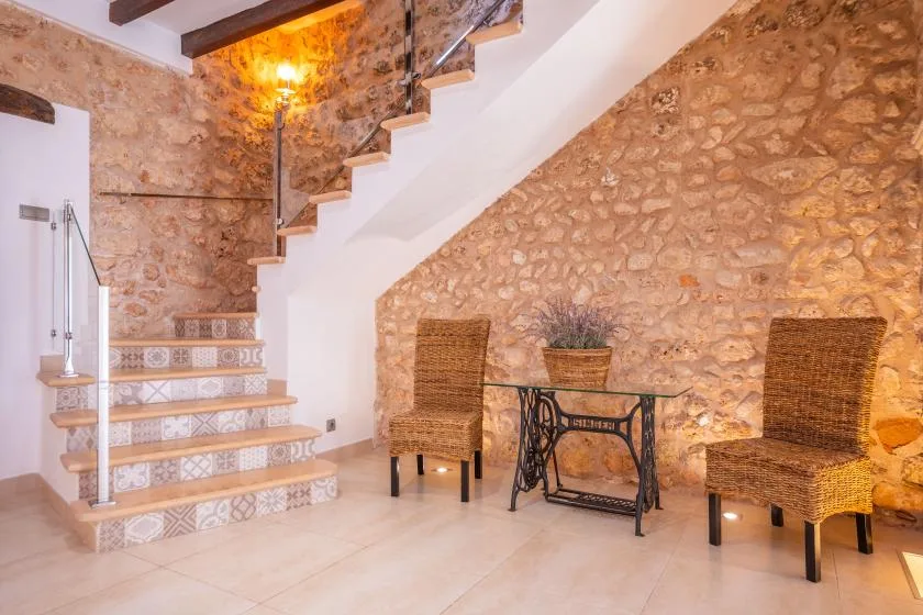A stone-walled interior with a tiled staircase, wicker seating, and a small table.