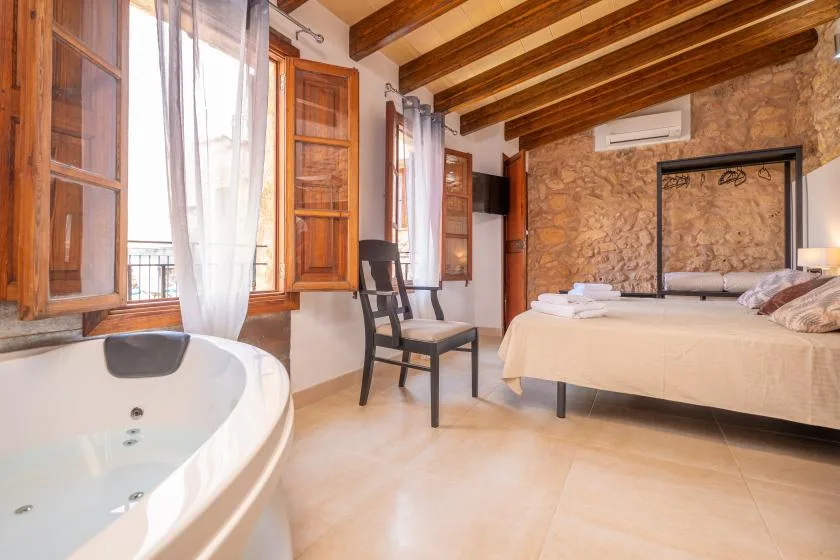 A bedroom with a bed, a chair, and a bathtub beside the windows.