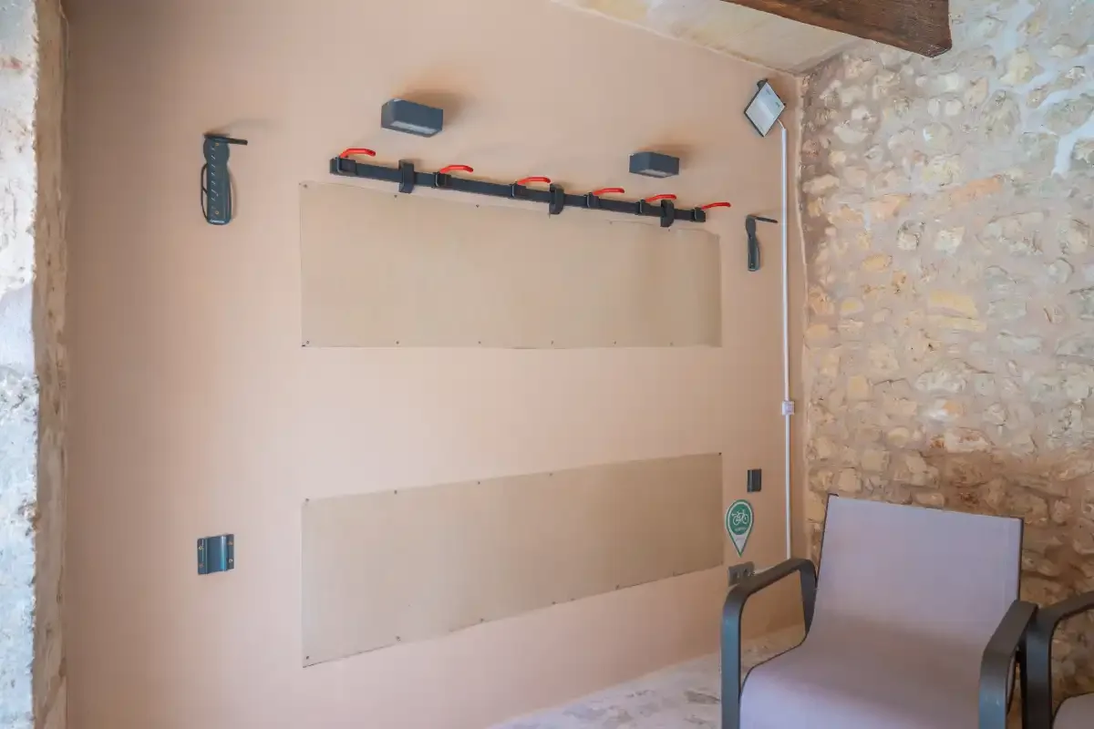 A pale wall with mounted fixtures and a chair in a stone-walled room.