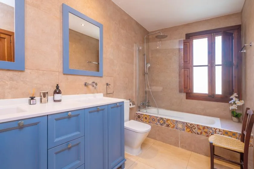 A bathroom with a blue vanity, bathtub, and window.