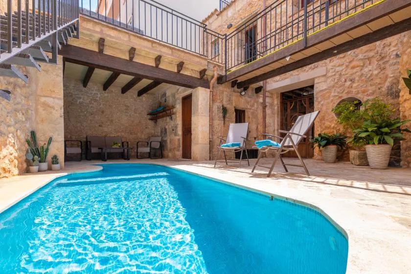 A courtyard pool sits beside stone walls, with seating and potted plants nearby.