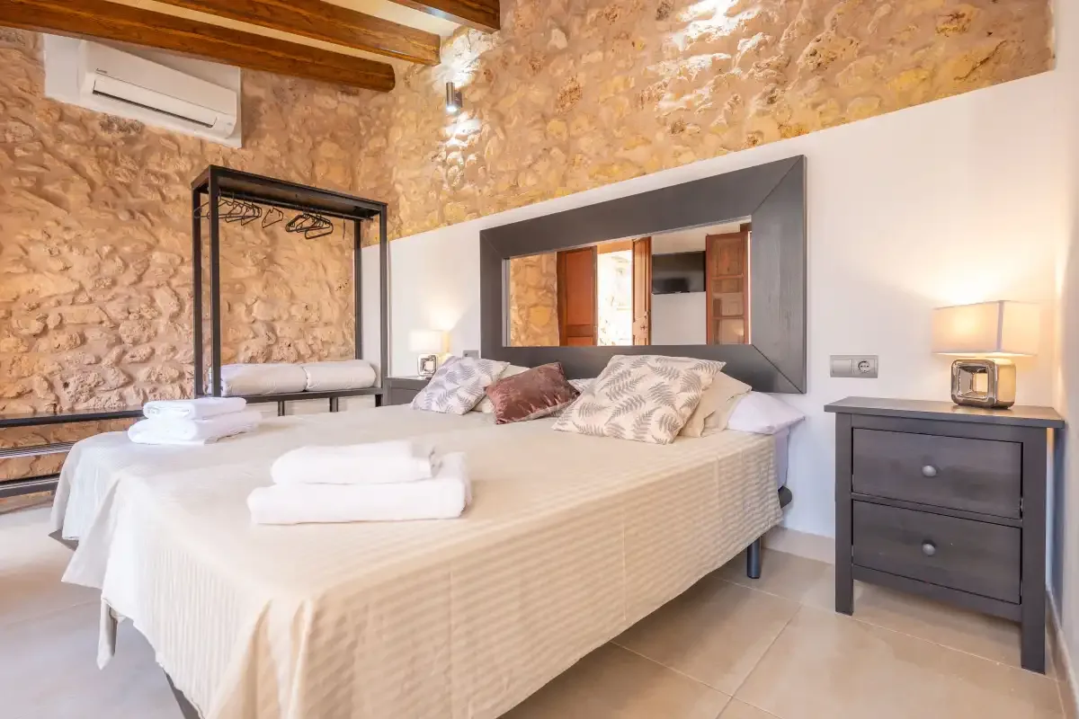 A bedroom with a large bed, exposed stone walls, and wooden ceiling beams.