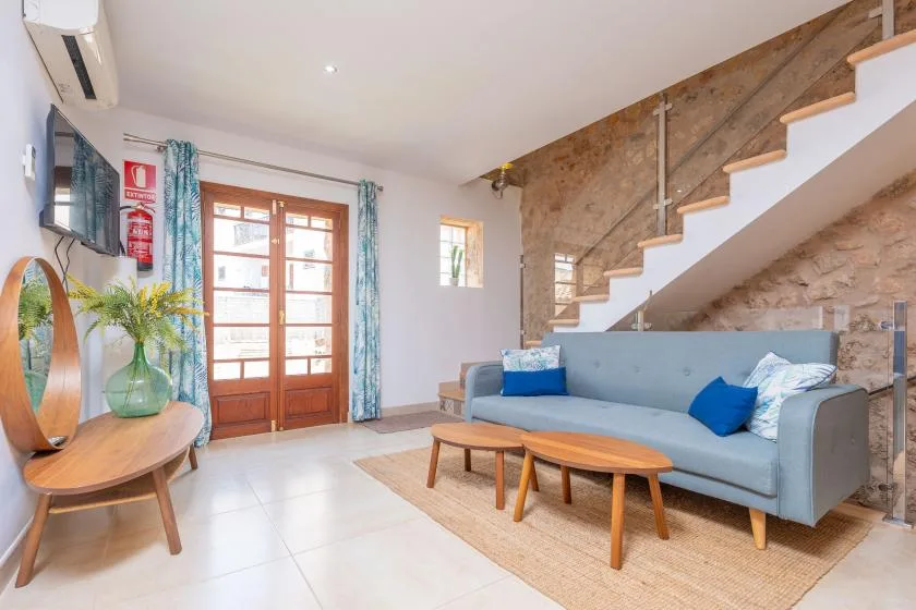 A living room with blue seating and a staircase along the stone wall.