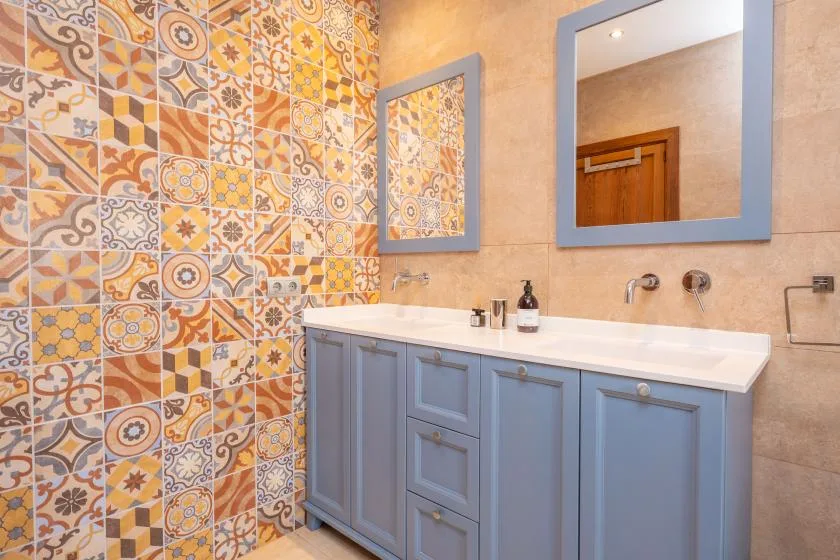 A bathroom vanity with blue cabinetry sits beside a wall of colorful patterned tiles.