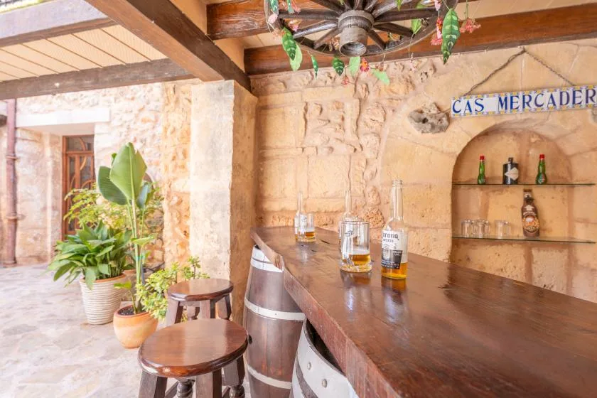 A rustic bar counter with stools, bottles, and stone walls.