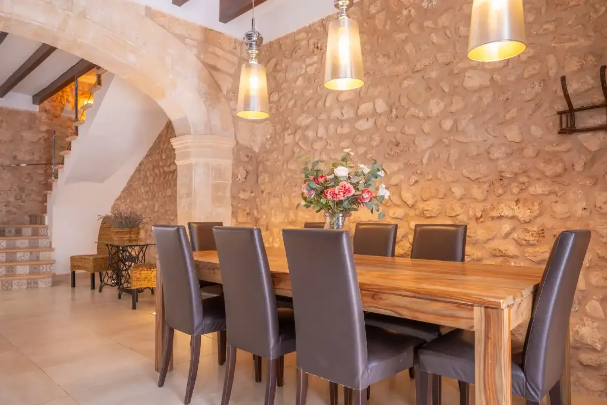 A dining room with a long wooden table and upholstered seating beneath pendant lights.