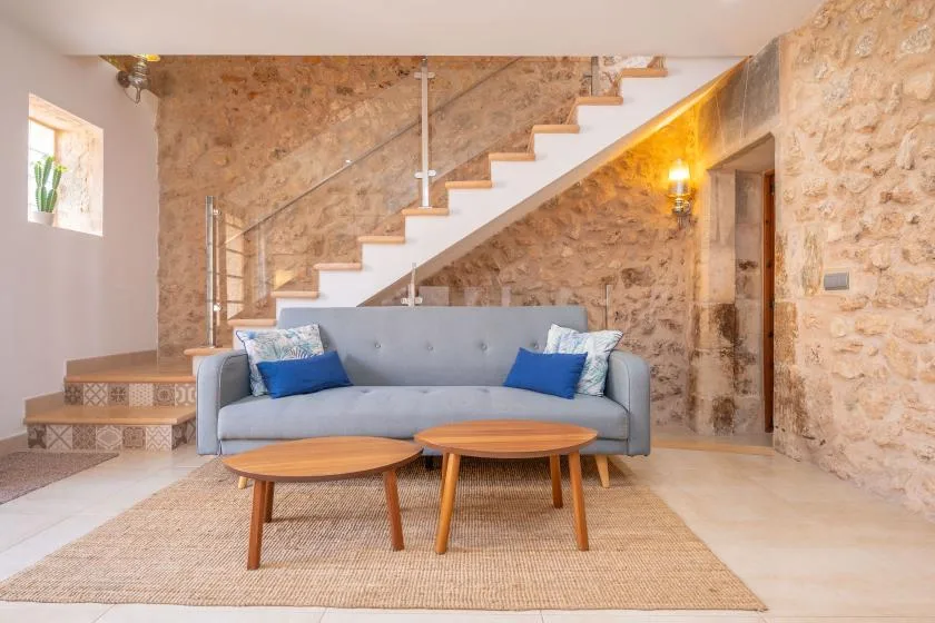 A living room with a gray sofa and wooden coffee tables beneath a staircase.