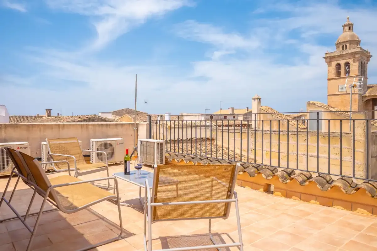 A rooftop terrace has seating beside a metal railing, with a church tower in the distance.