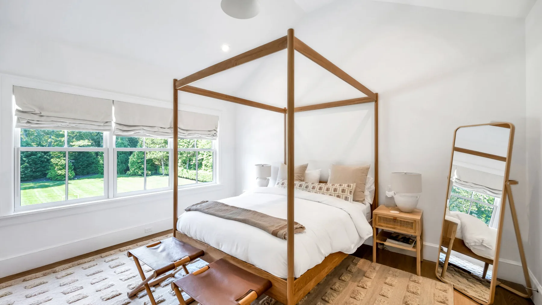 Un dormitorio luminoso con una cama con dosel de madera y grandes ventanas con vistas a la vegetación.