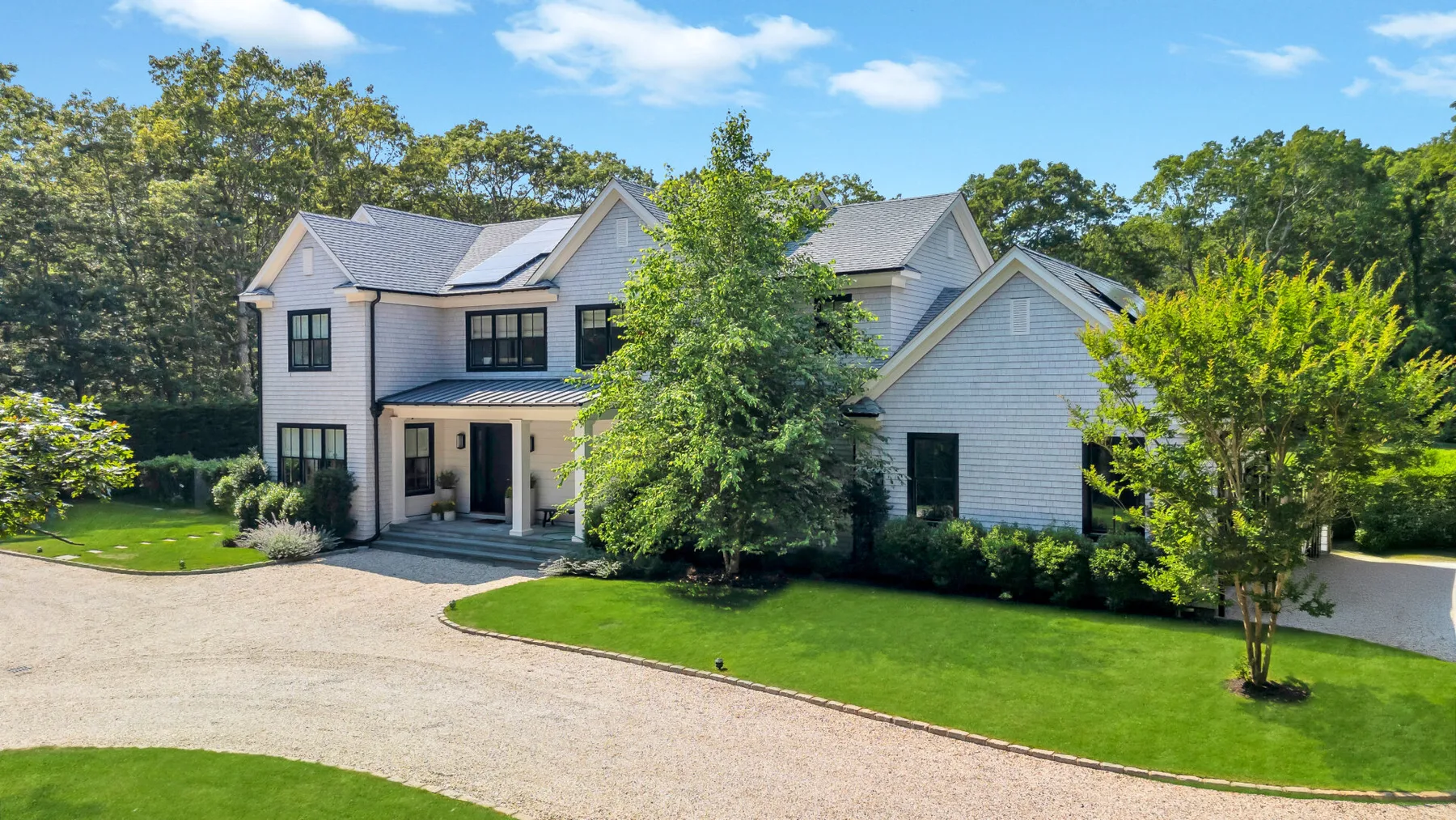 A large house stands beside a curved gravel driveway and green lawn.