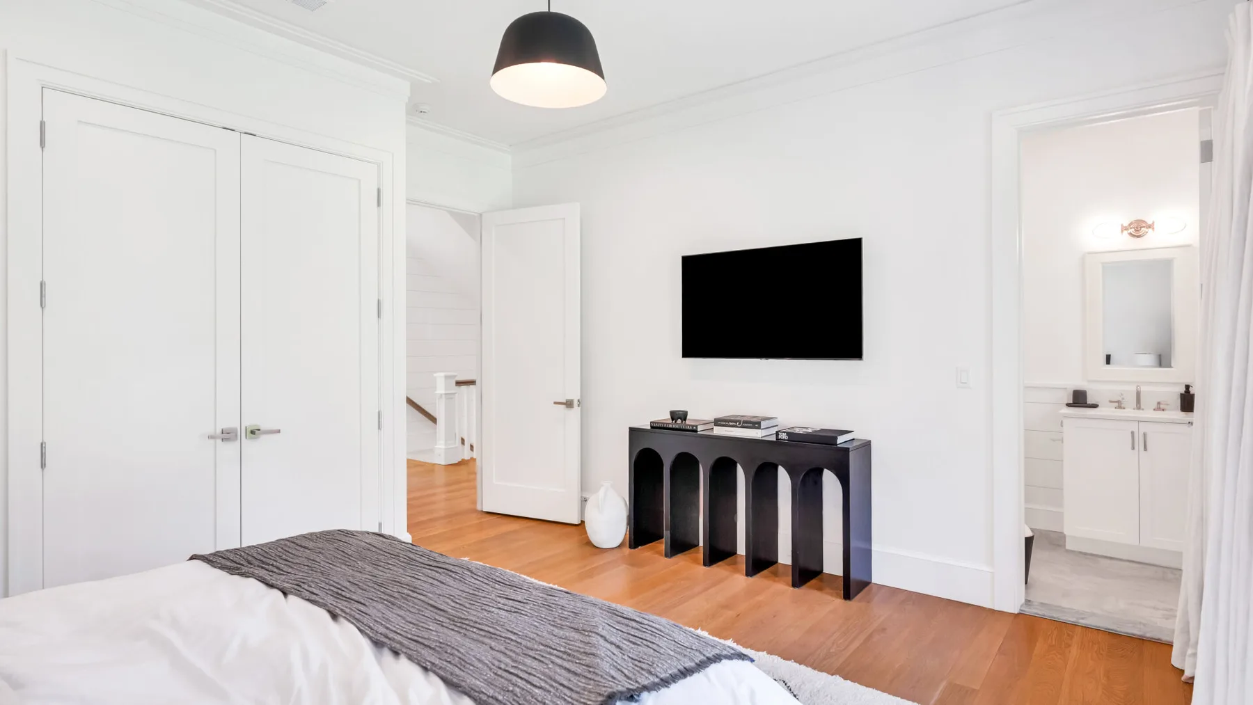 Un dormitorio luminoso con un televisor sobre una consola oscura y una puerta abierta.