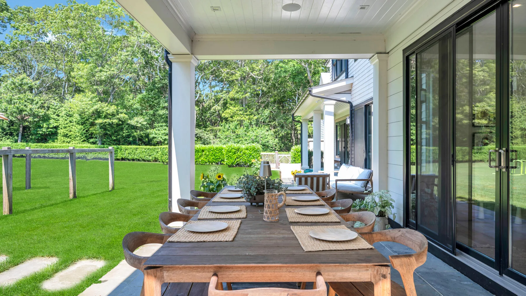 Un comedor exterior cubierto con una mesa larga junto a un césped verde.