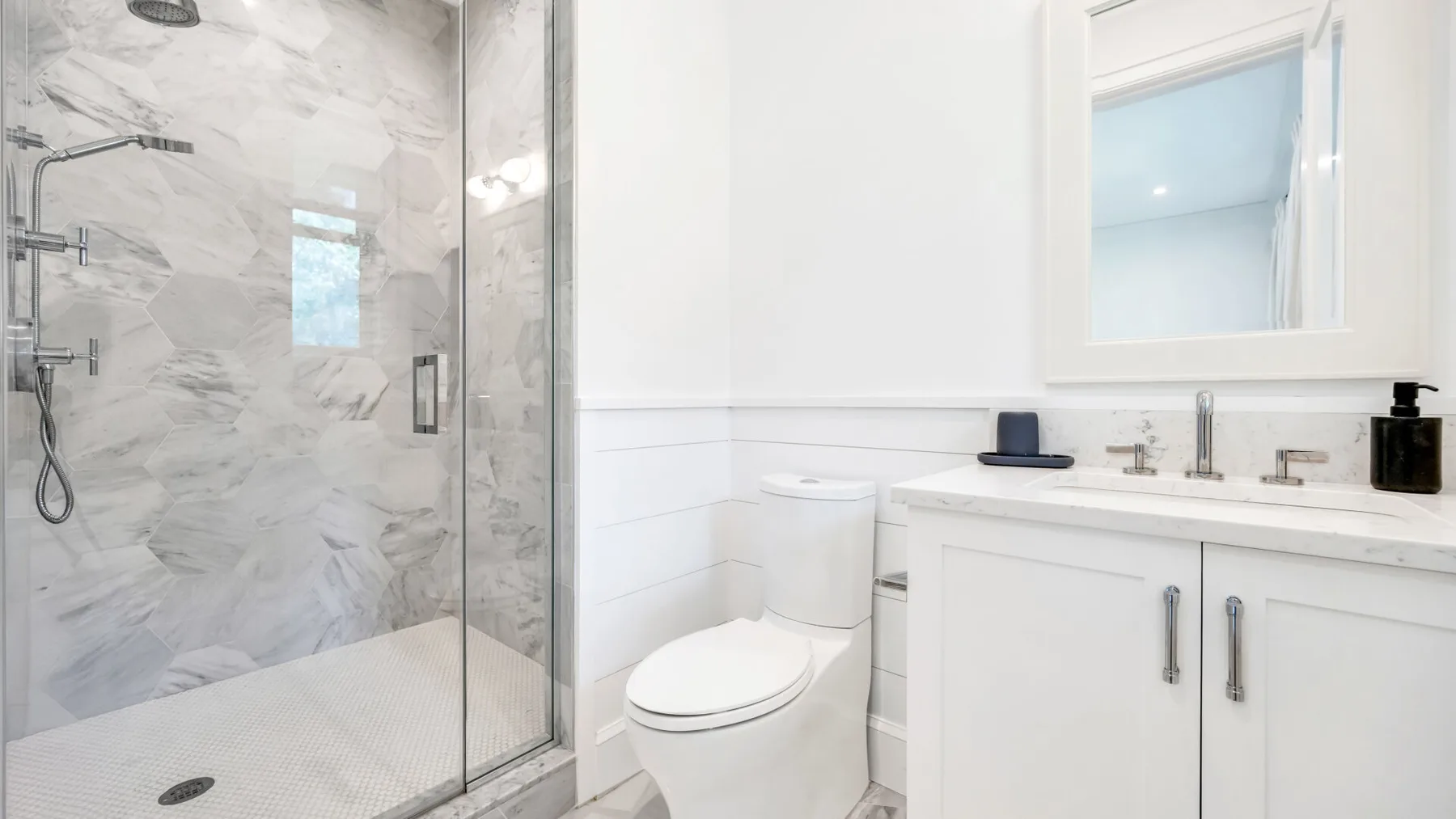 Un baño luminoso con ducha de vidrio y un mueble de lavabo blanco.