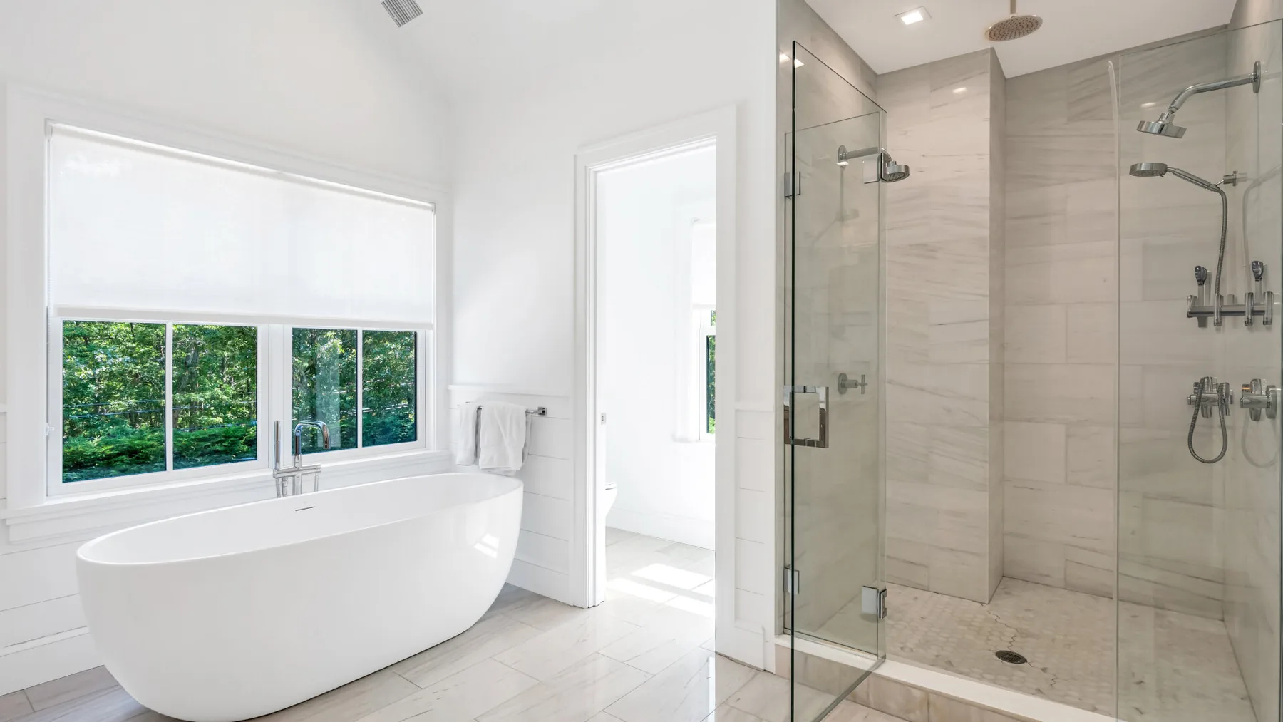Un baño luminoso con una bañera exenta junto a una ducha de cristal.
