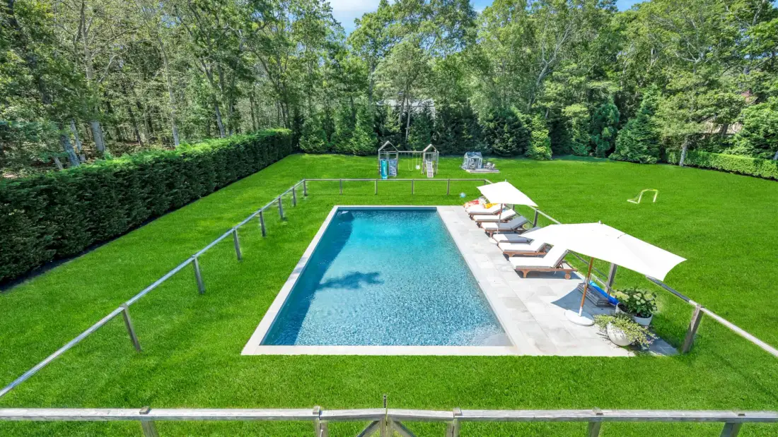 Una piscina está rodeada de césped y árboles.