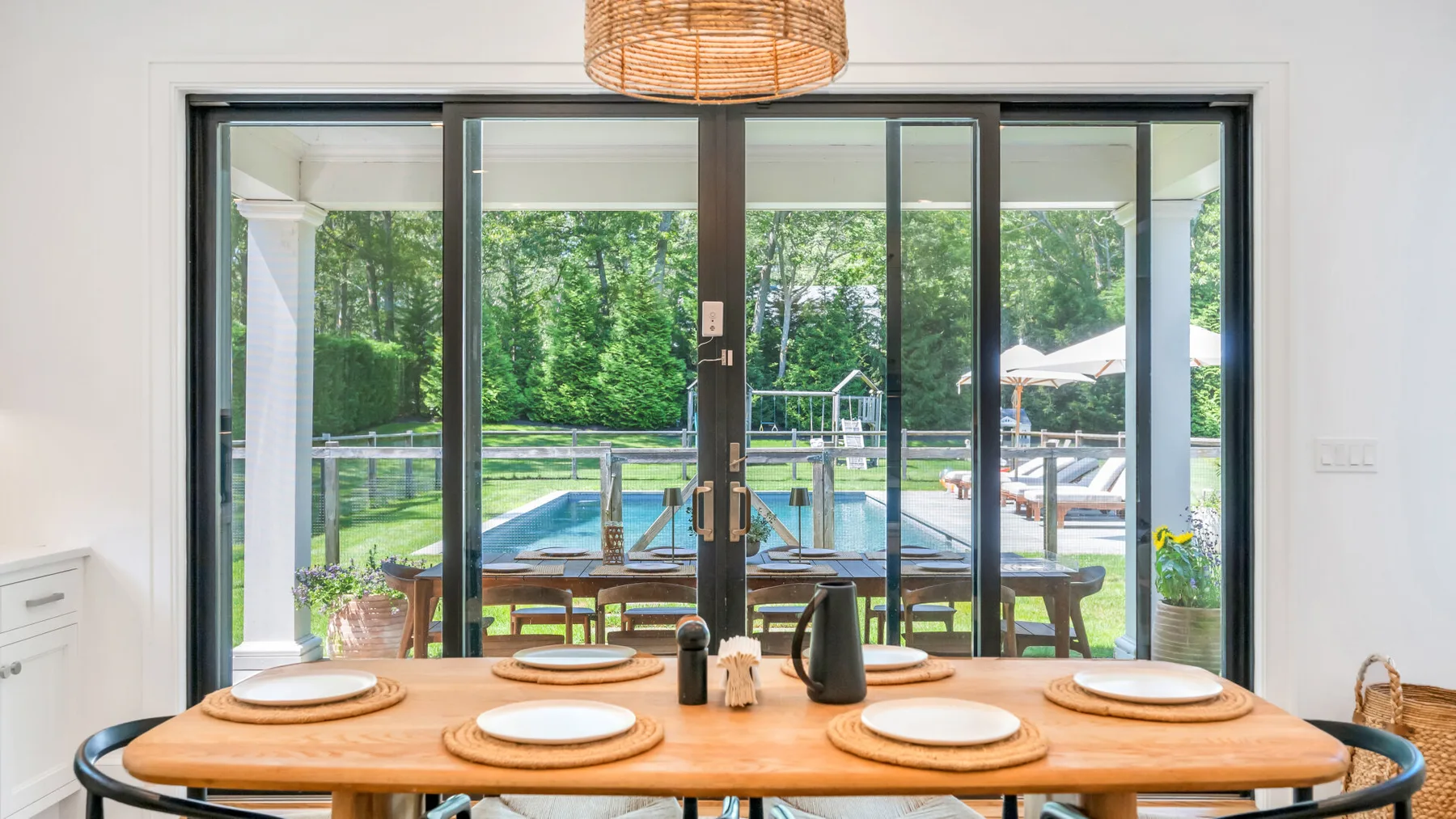 Una mesa de comedor da a grandes puertas de vidrio con vistas a una piscina y un jardín verde.