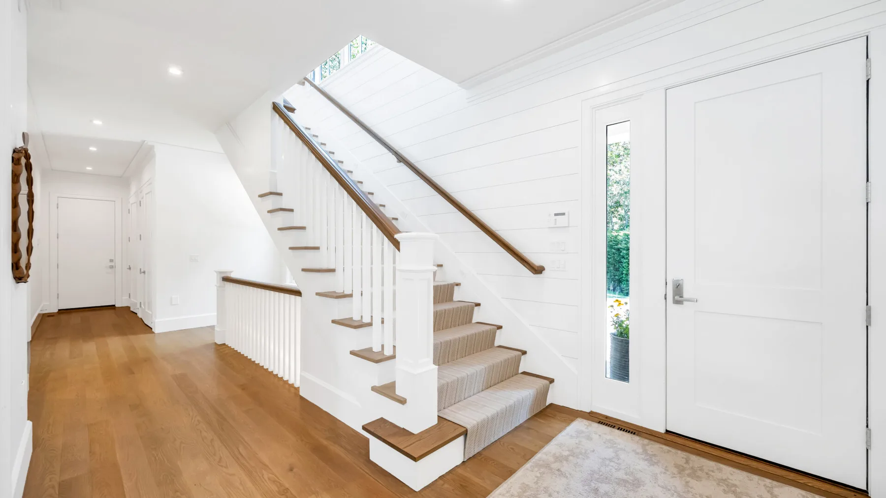 Un recibidor luminoso con una escalera y una puerta de entrada blanca.