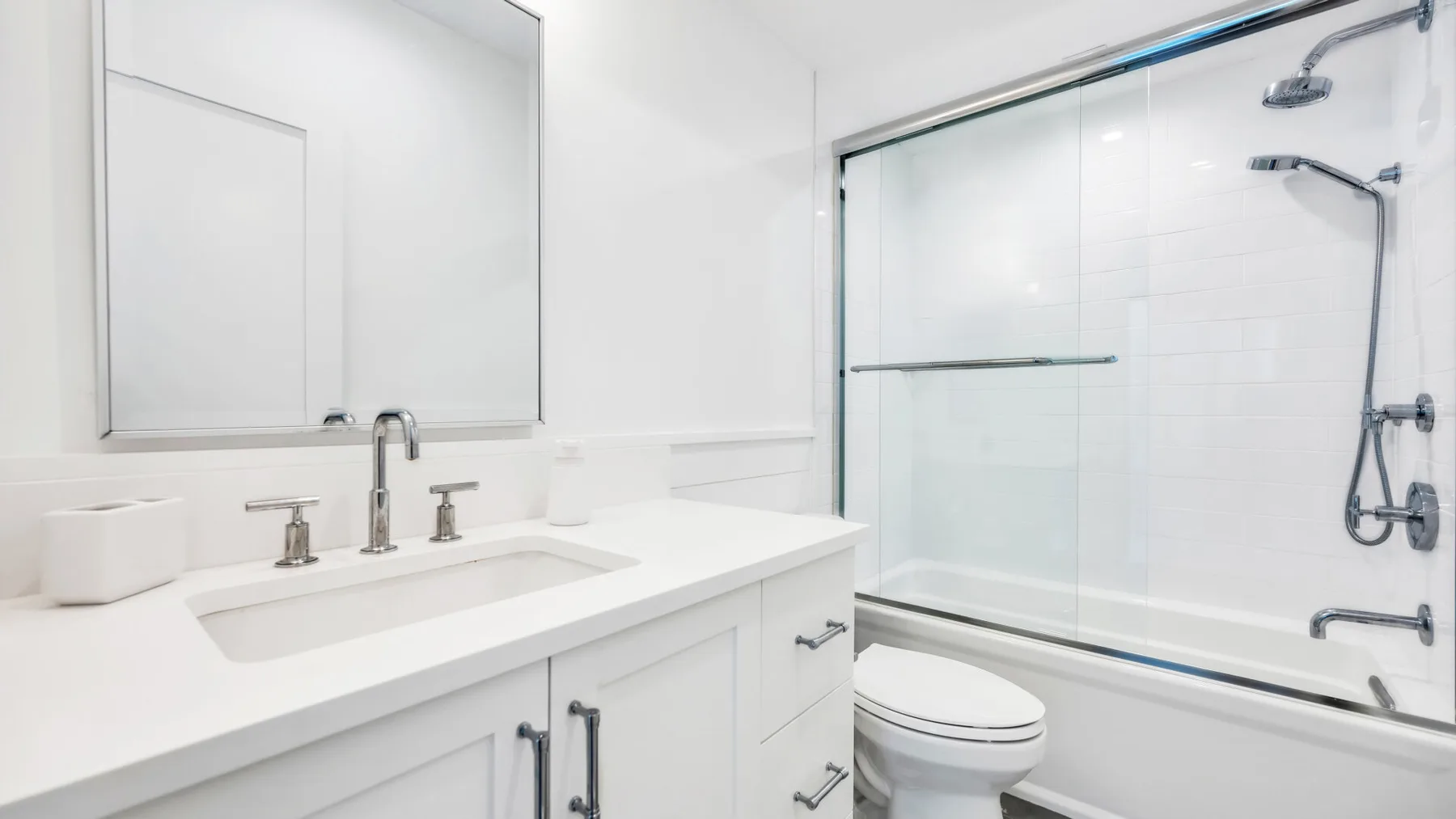 Un baño luminoso con lavabo, inodoro y bañera con panel de vidrio.