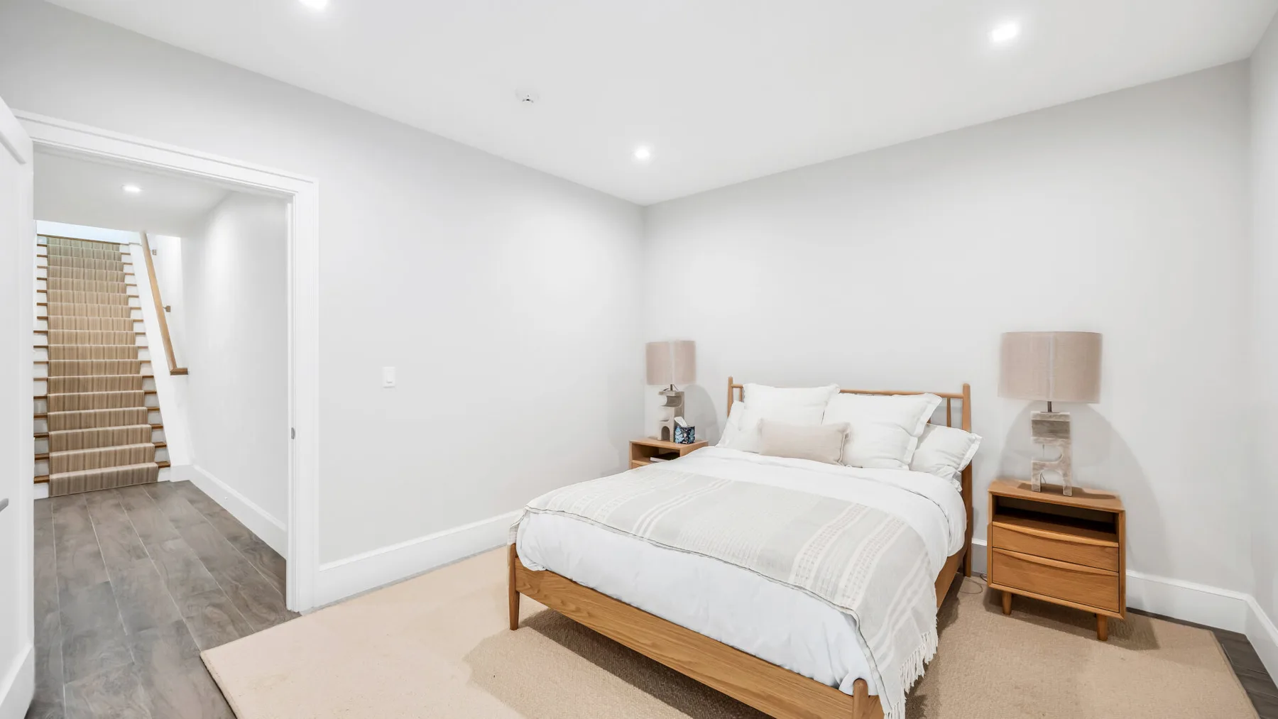 Un dormitorio luminoso con una cama tendida y una puerta abierta hacia una escalera.