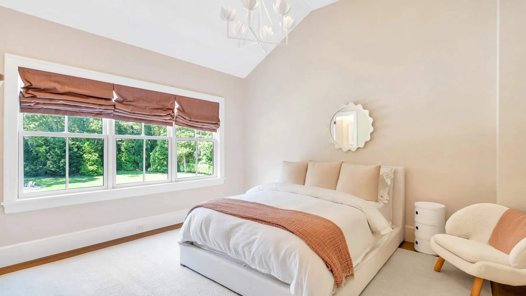 Un dormitorio luminoso con una cama junto a amplias ventanas con vistas a la vegetación.