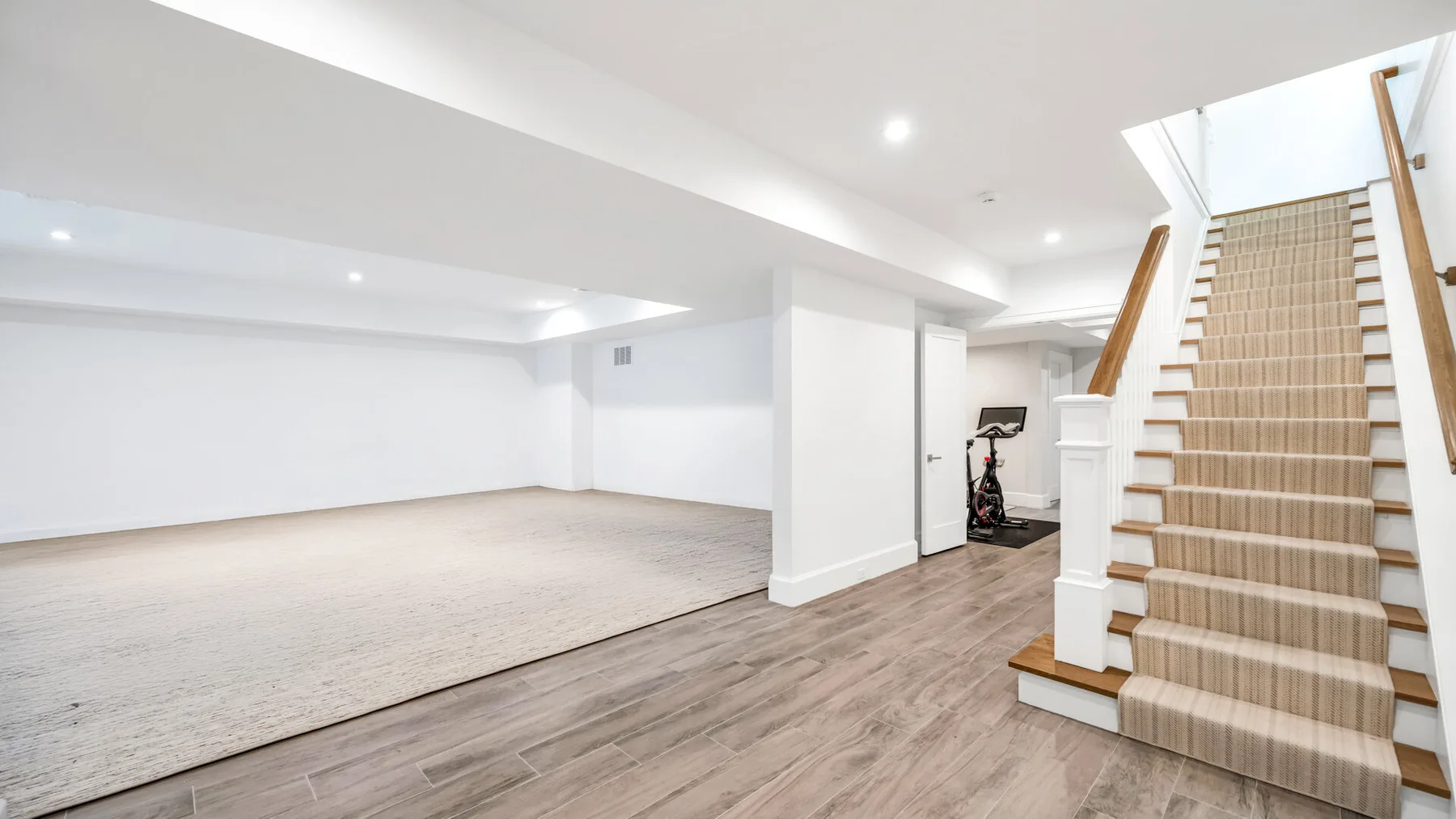 Una luminosa sala en el sótano con alfombra y una escalera.