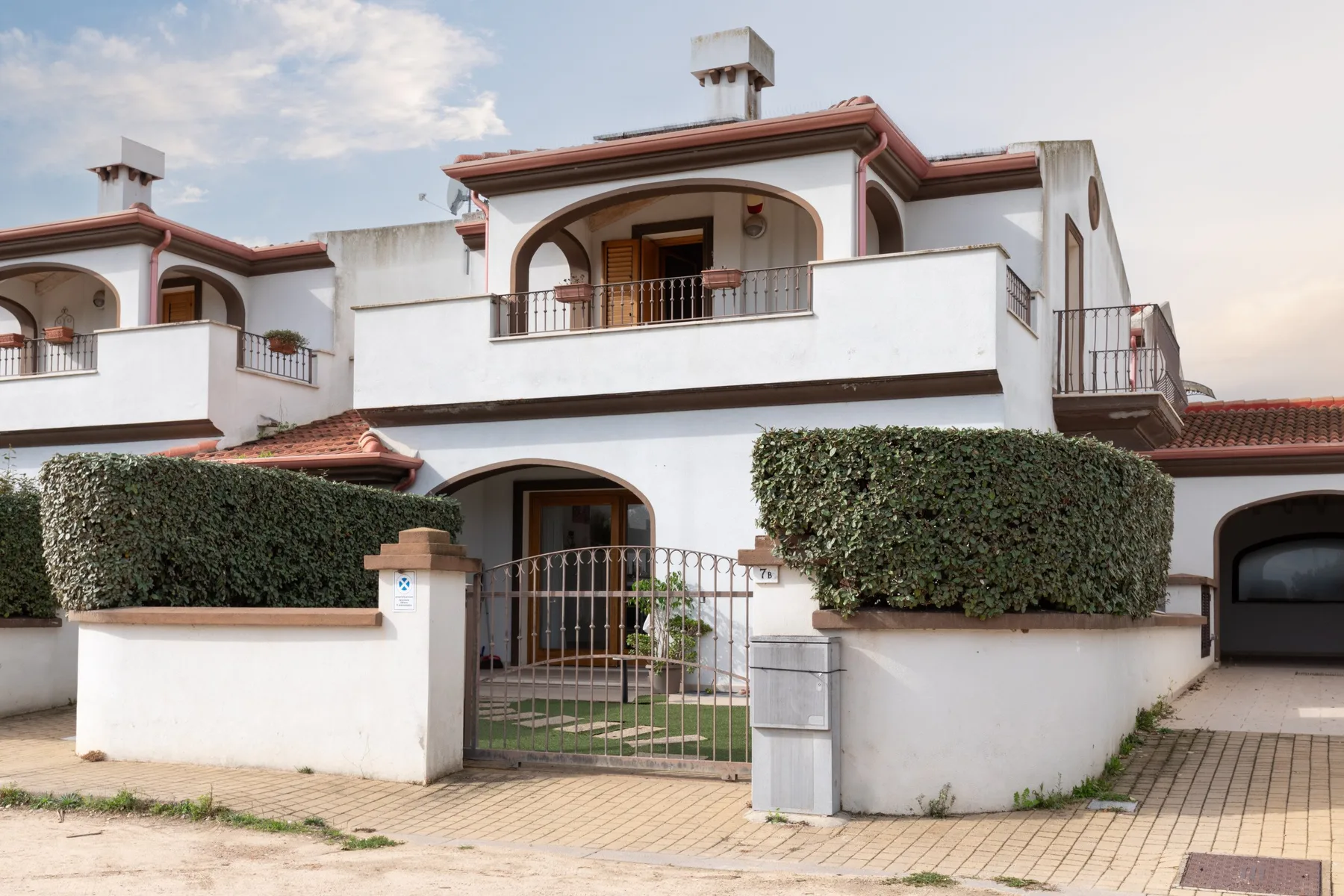 Edificio blanco de dos plantas con balcones arqueados y una entrada con reja.