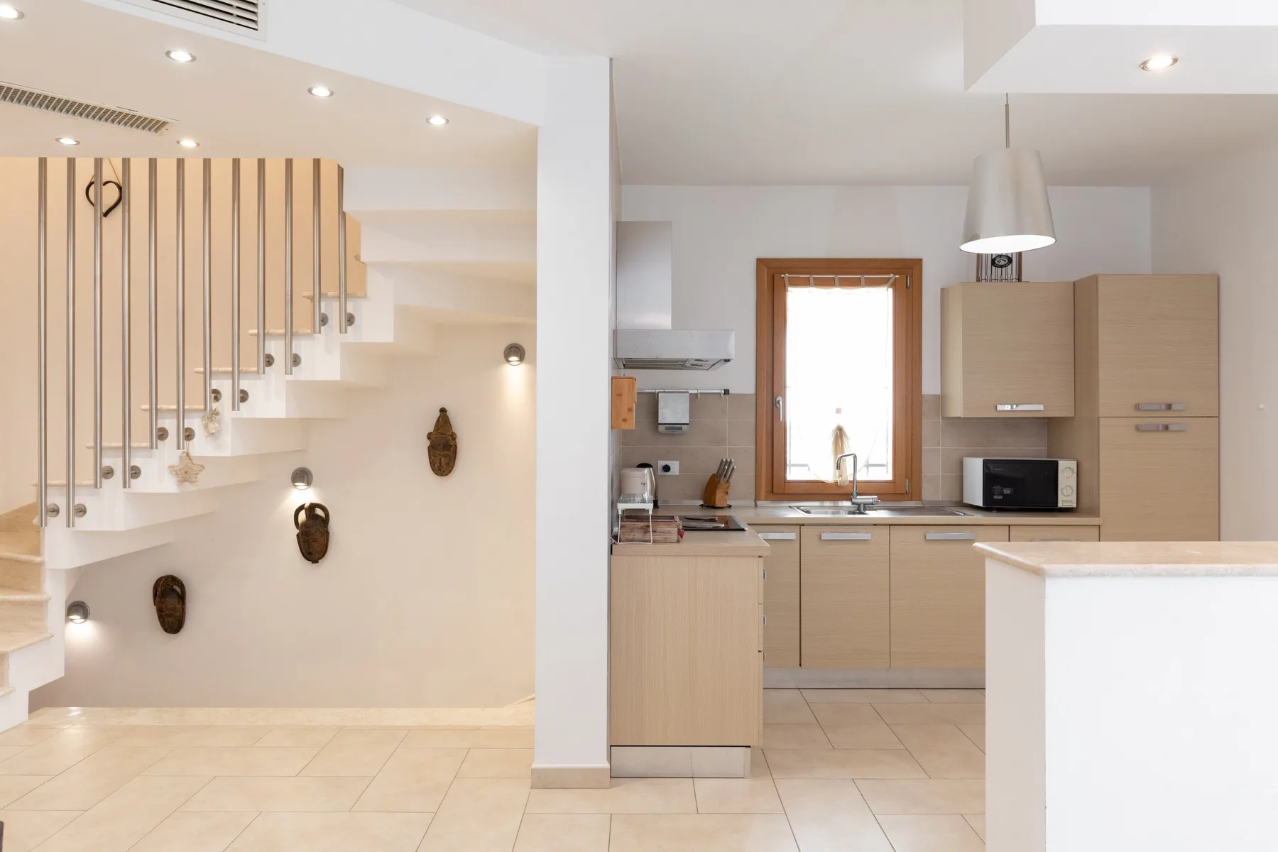 Una cocina luminosa junto a una escalera, con gabinetes claros e isla central.