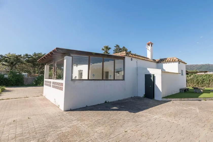A white single-story building with a large glazed veranda faces a paved courtyard.