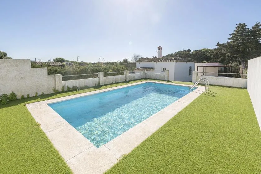 An outdoor swimming pool is surrounded by a paved border and green lawn.