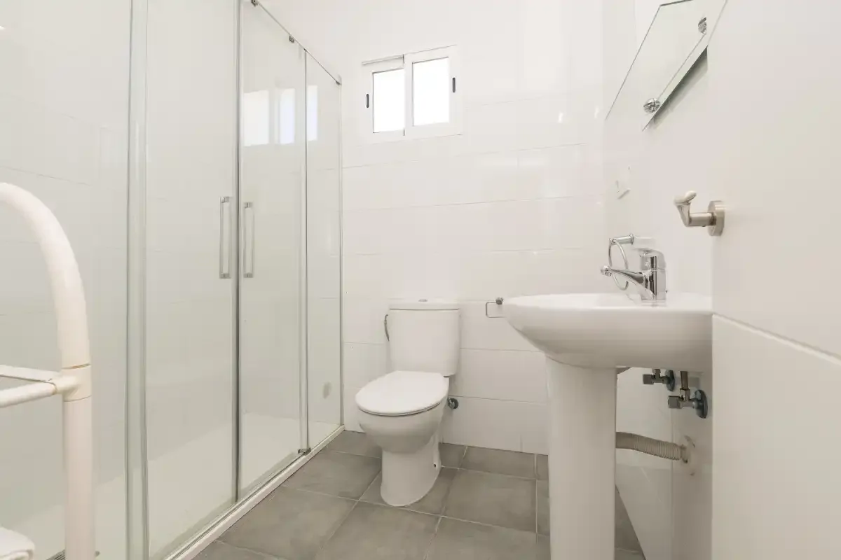 A bright bathroom with a glass shower, toilet, and pedestal sink.