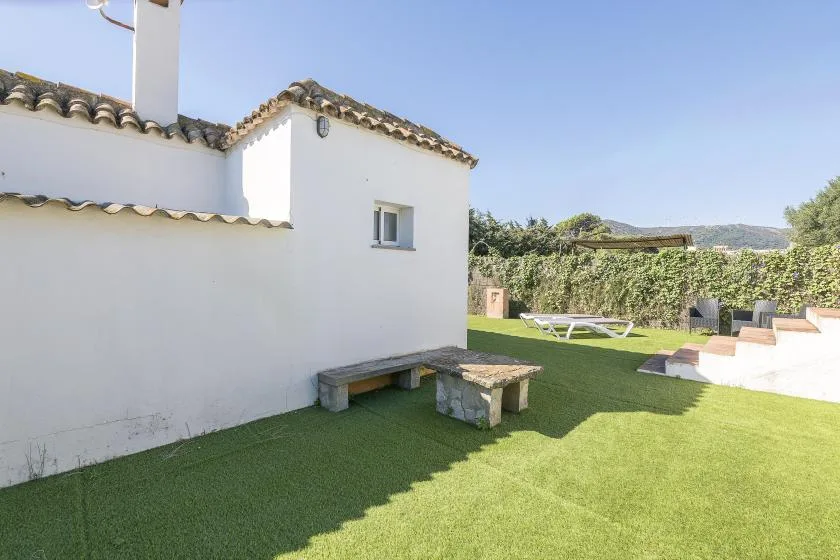 A grassy outdoor patio beside a white building, with lounge seating and a low table.