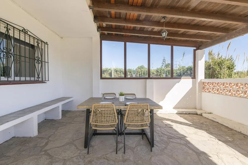 A covered patio with a dining table and chairs overlooks a garden.