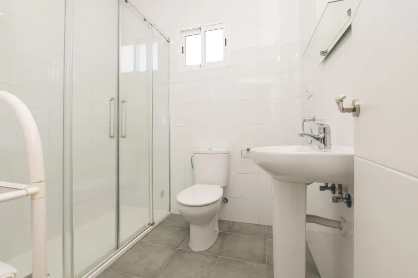 A bright tiled bathroom with a glass shower, toilet, and pedestal sink.