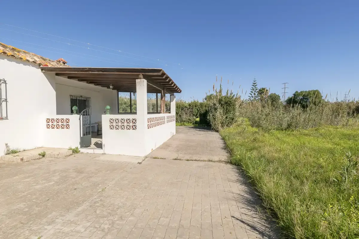 A paved driveway leads past a small white building and grassy field.